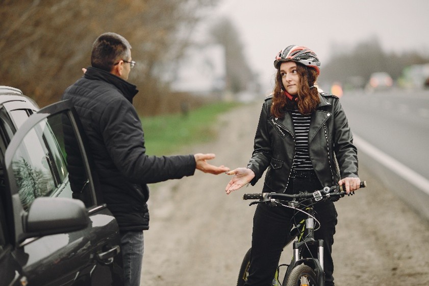 Man zit op de weg na een val met zijn fiets, zichtbaar met pijn, terwijl zijn fiets en helm naast hem liggen.
