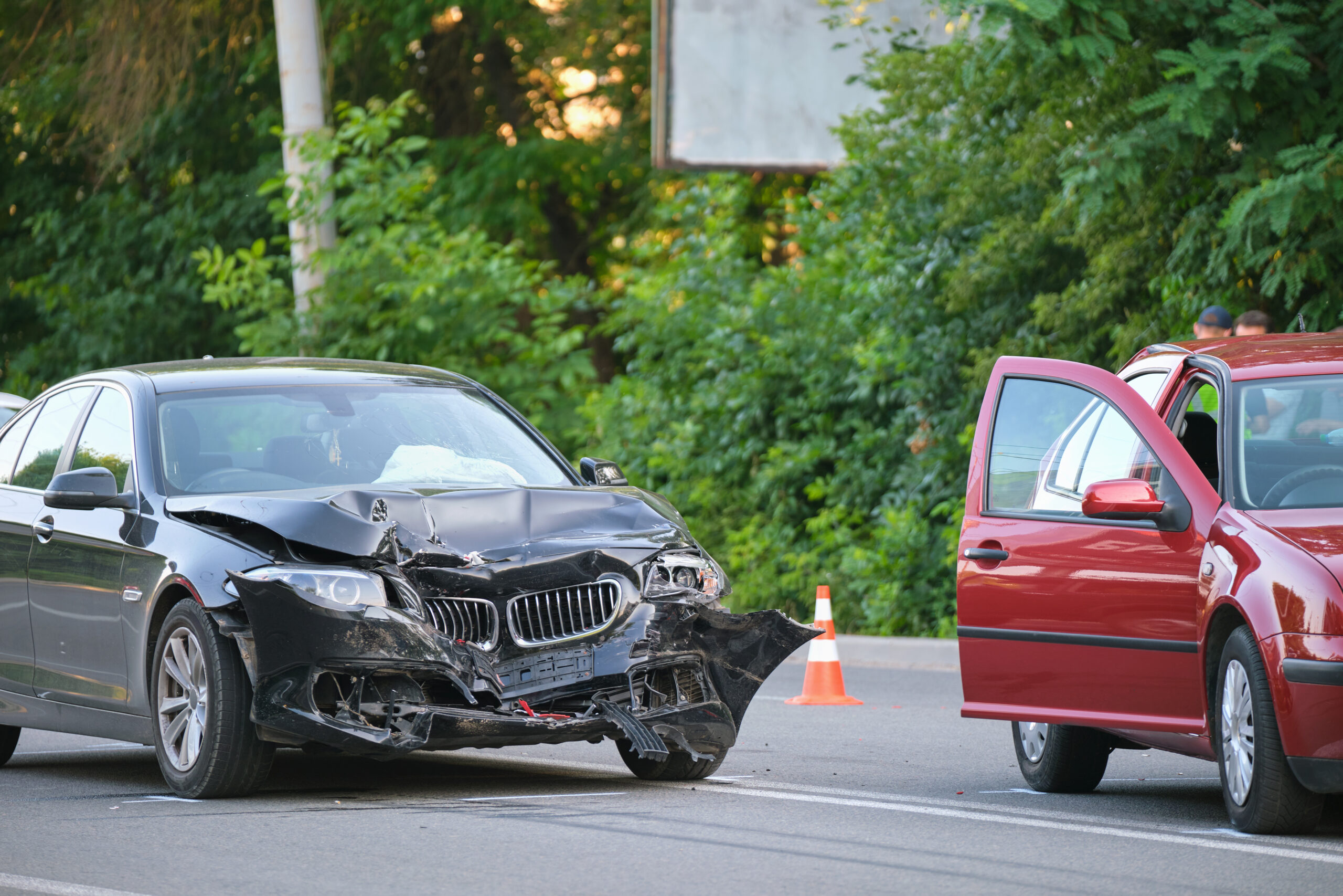 Twee auto’s met schade na een botsing op de weg, met open portier en verkeerskegel bij de plaats van het ongeval.
